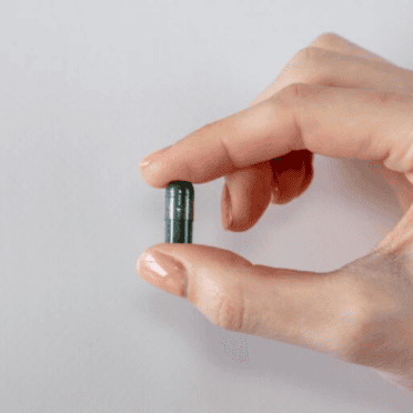 woman's hand holding one Love CBD Entourage Capsules in front of grey background