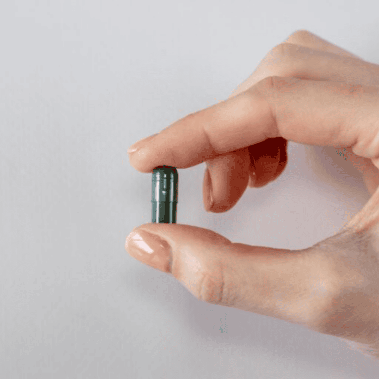 woman's hand holding one Love CBD Entourage Capsules in front of grey background