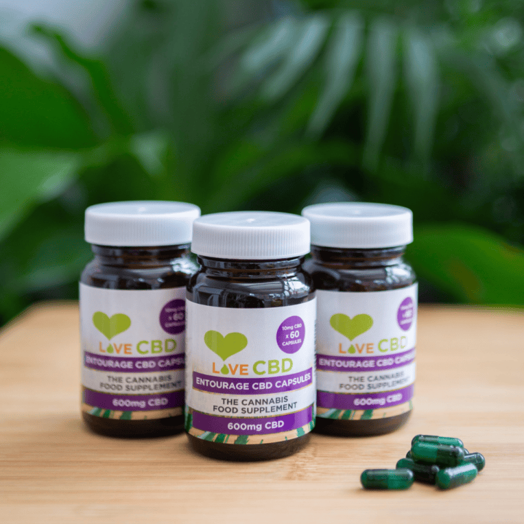Love CBD Entourage Capsules three bottles with capsules on table plant background