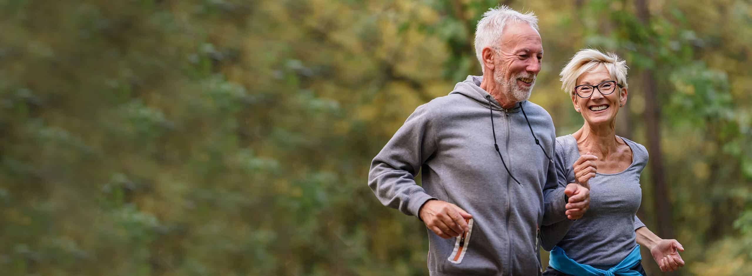 Cheerful active senior couple jogging in the park.