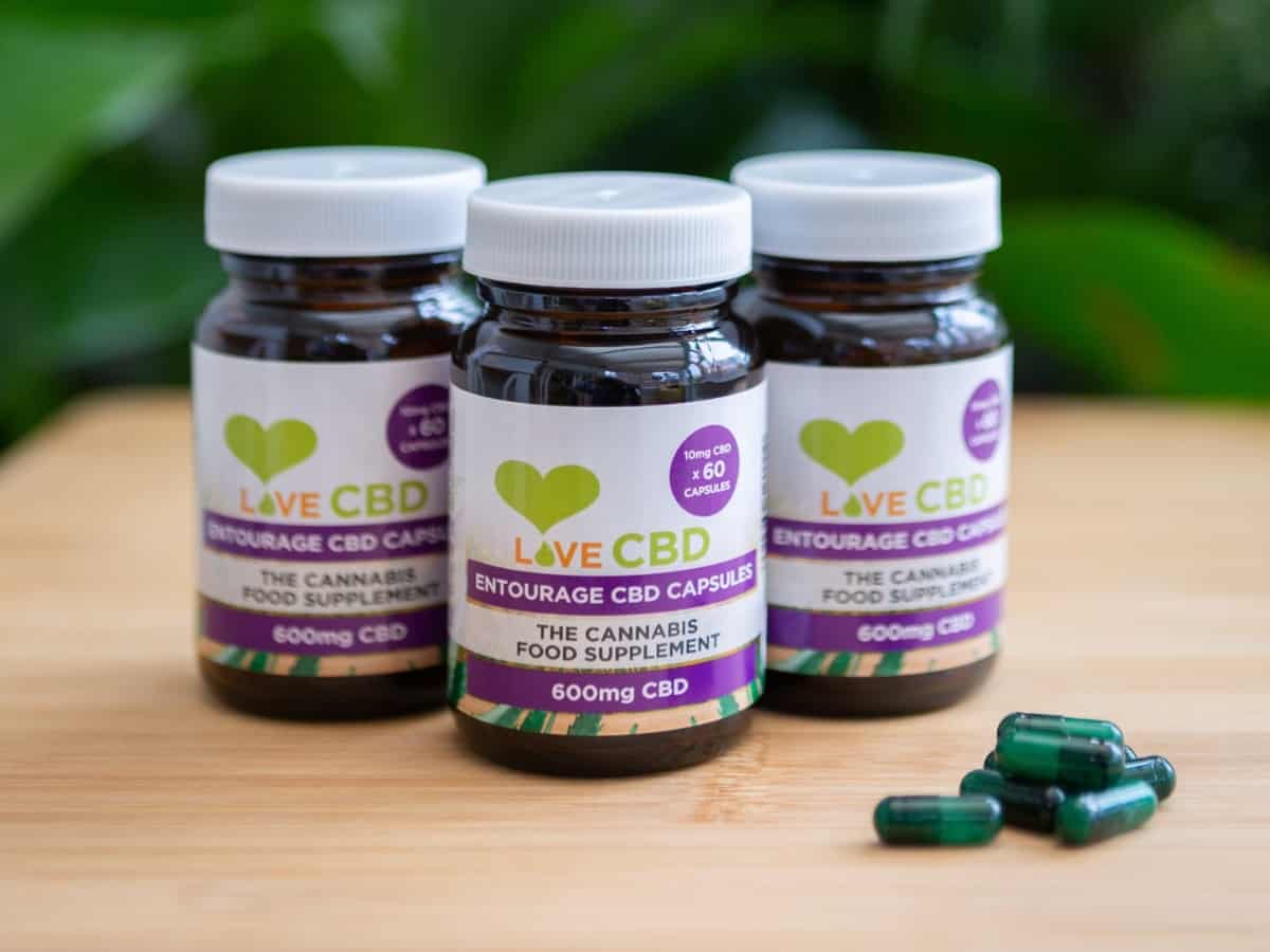 Love CBD Capsules with bottles on table leafy background