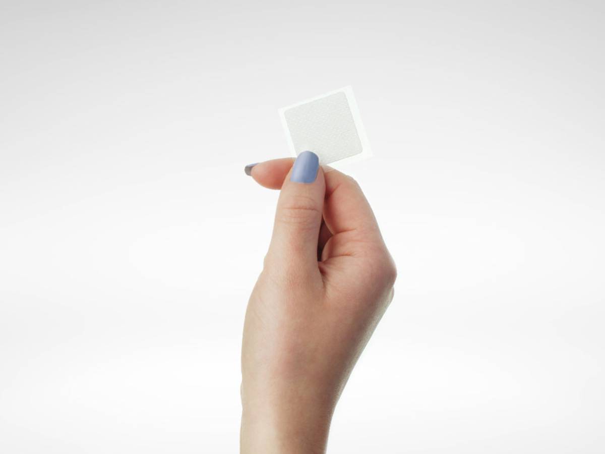 Female with blue nail paint on holding a CBD patch in front of a white background