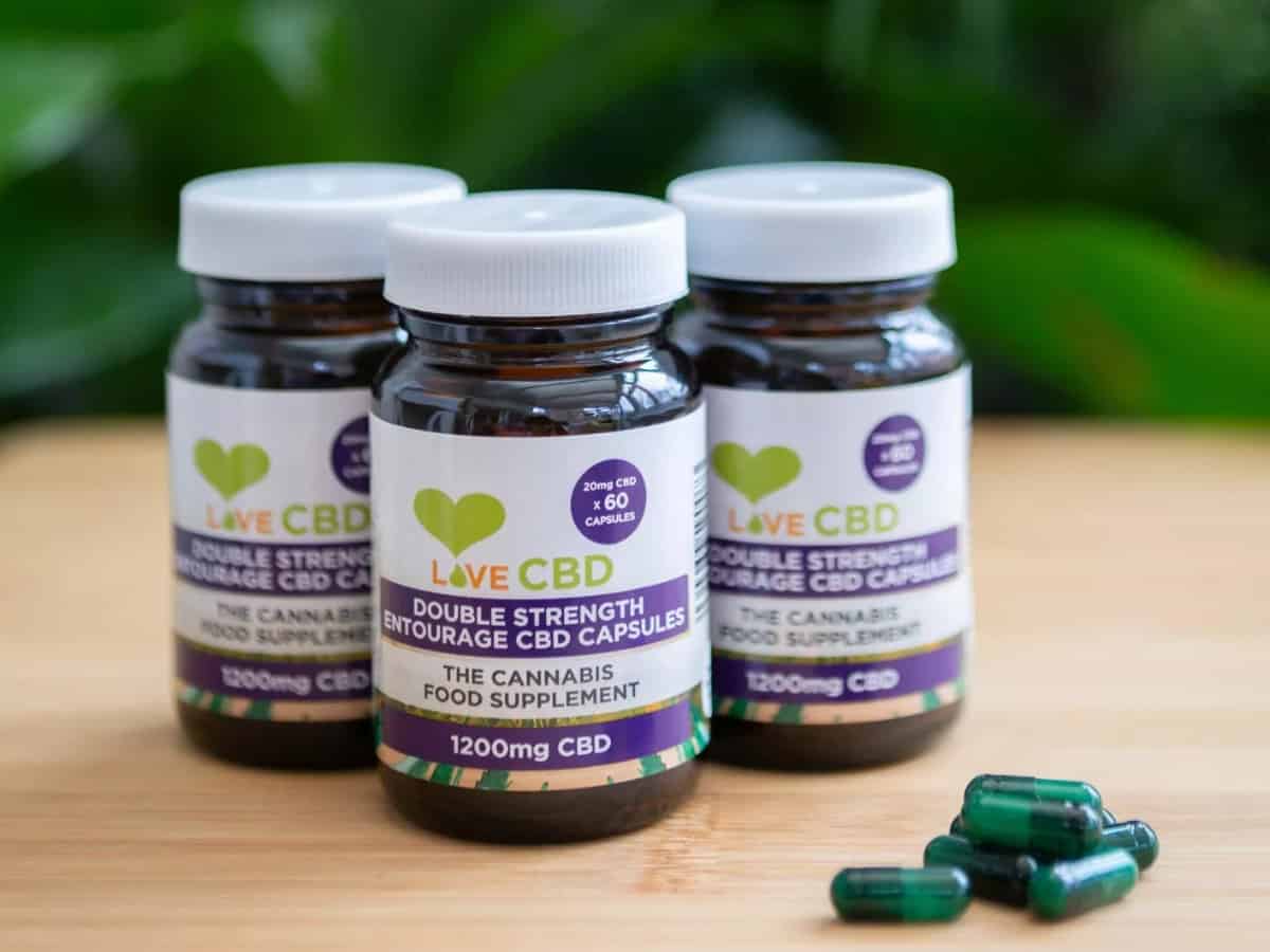 3x Love CBD Entourage Capsules Double Strength on table with capsules leaf background