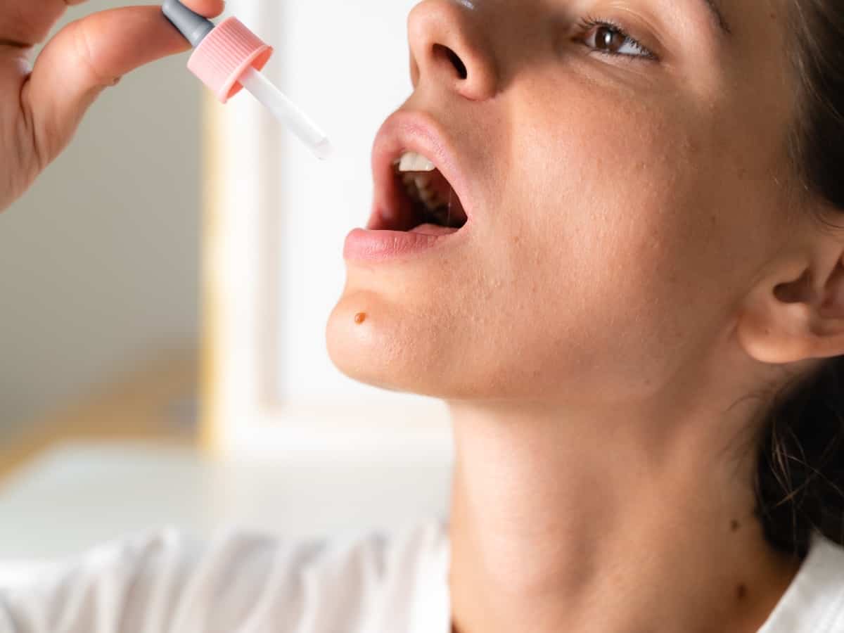 Woman with white t-shirt taking CBD oil sublingually from a pink and clear pipette