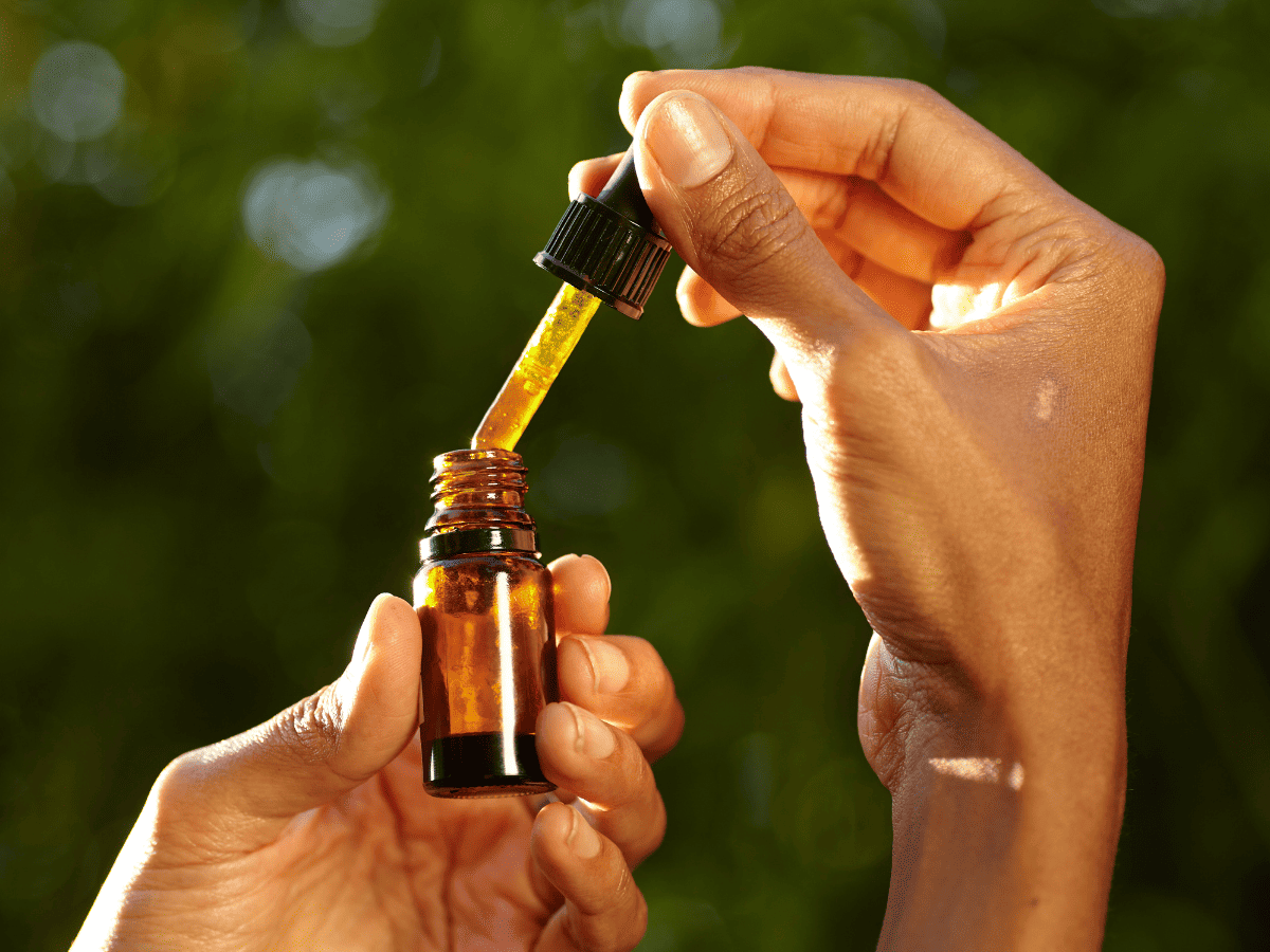 hands holding a bottle of cbd oil against a green leafy background