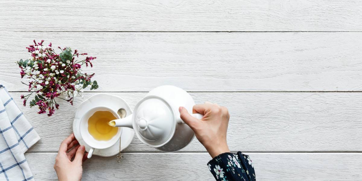 someone pouring tea into mug on a wooden table with flowers