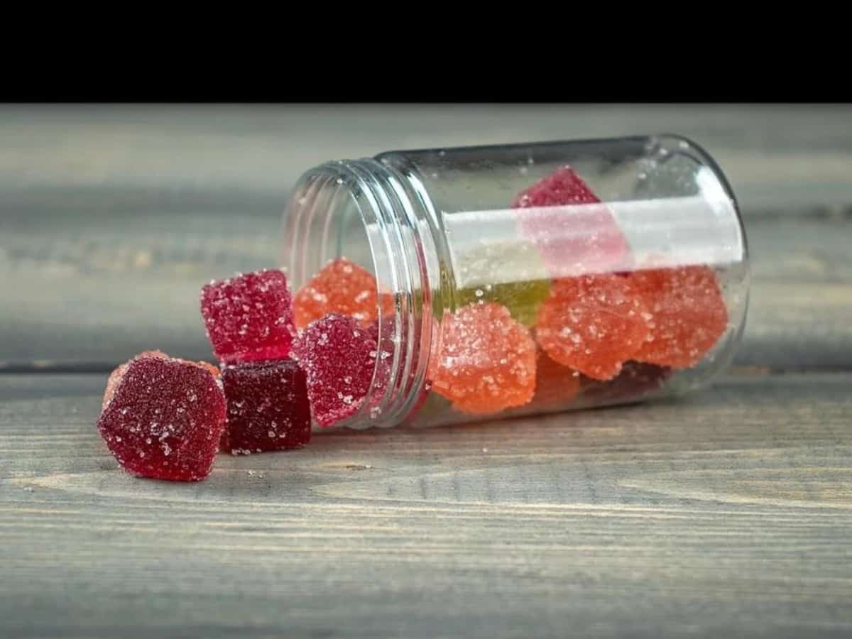 a glass jar of cbd gummy cubes spilt on a wooden table