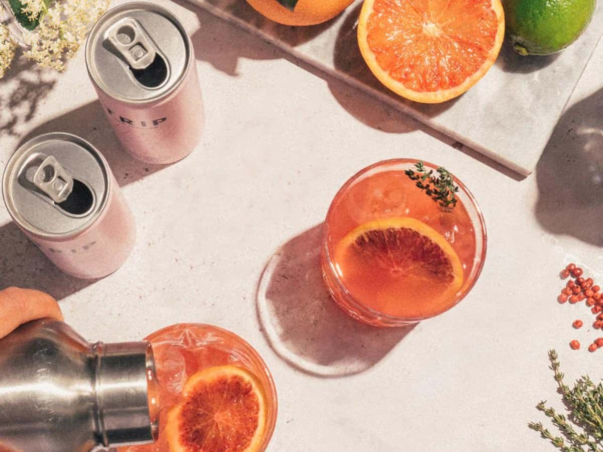 two trip cbd drinks and glasses of orange beverages surrounded by flowers and orange halves