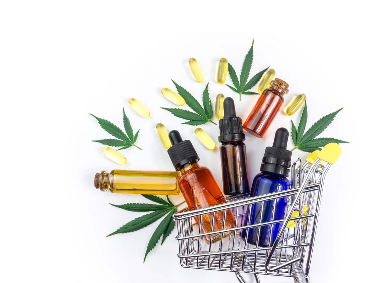 a mini-shopping trolley with bottles of cbd oil and some cbd capsules taken from a birds eye view, with hemp leaves around it
