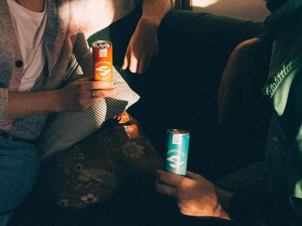 two people sat on a sofa in dim lighting, enjoying cans of goodrays cbd drinks