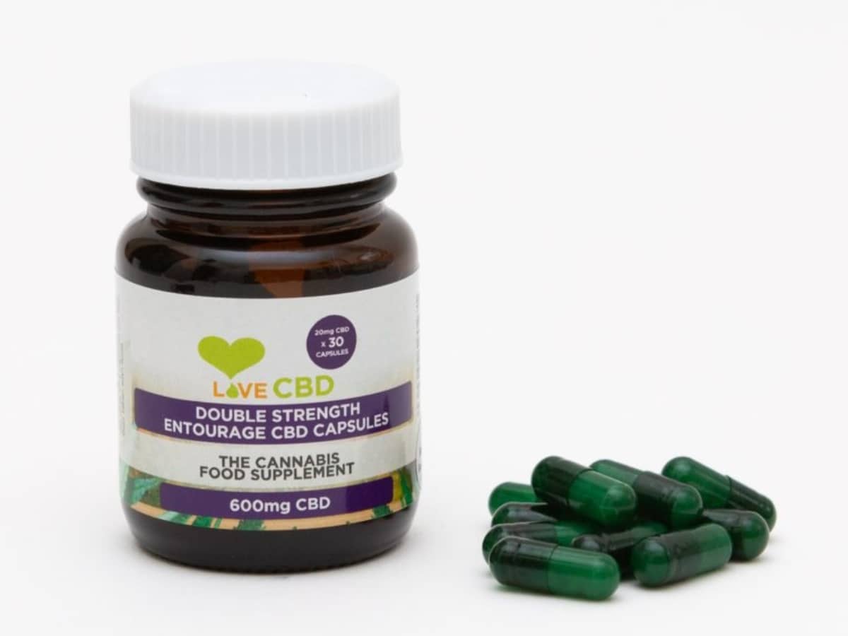 Love CBD Double Strength Entourage Capsules with pile of capsules beside bottle white background