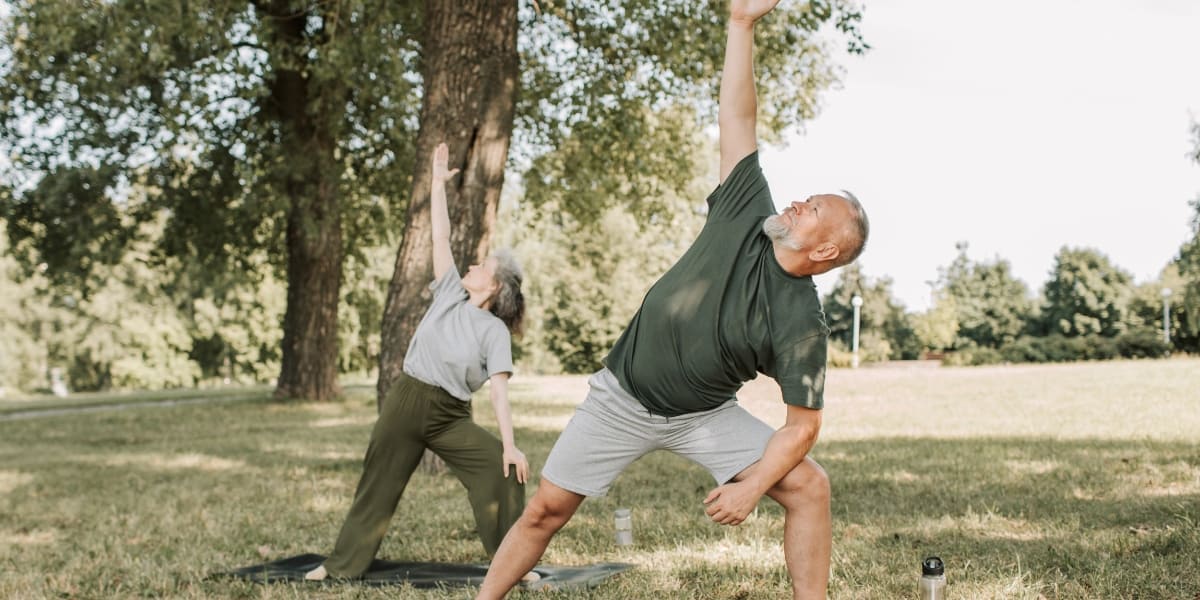 two seniors stretching and exercising in a park with greenery