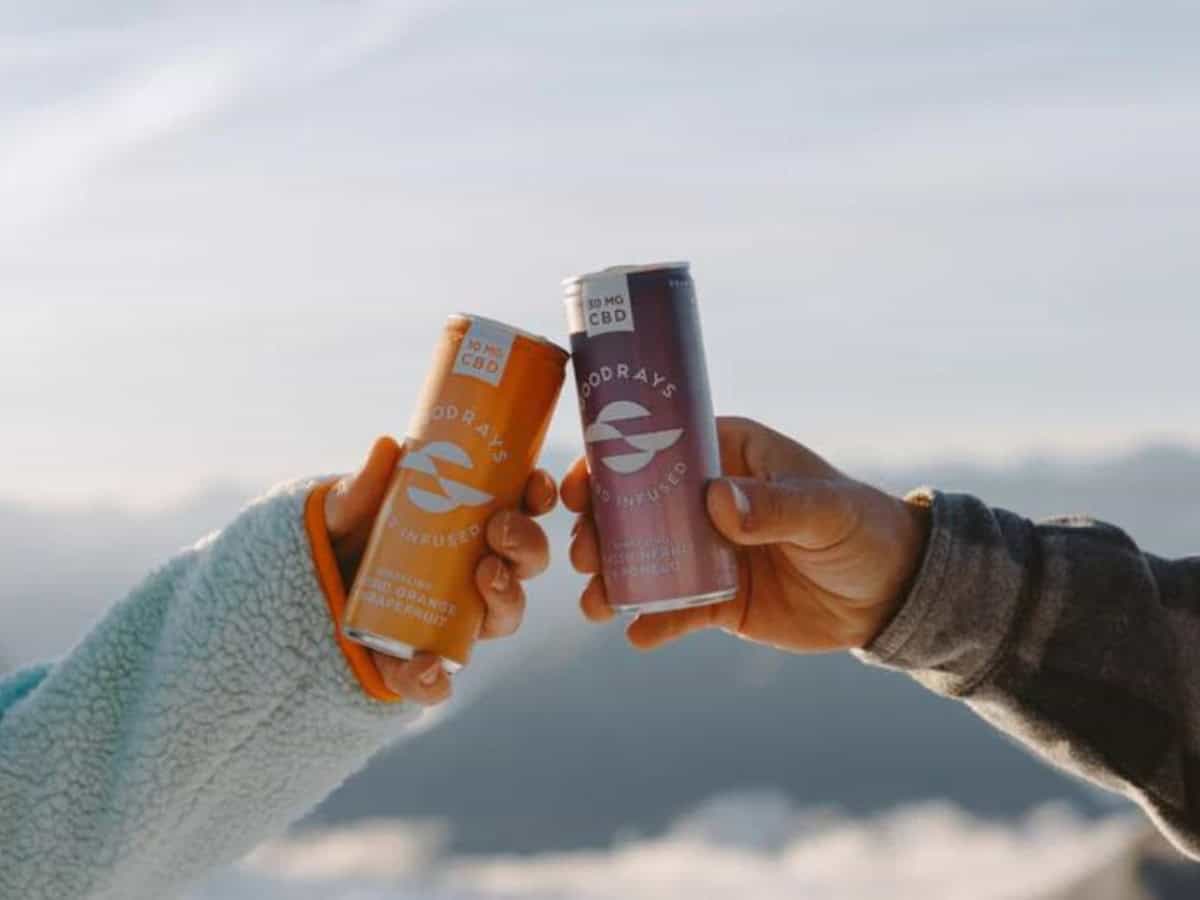 two hands cheersing cans on goodrays cbd drinks with a skyline and clouds in the background