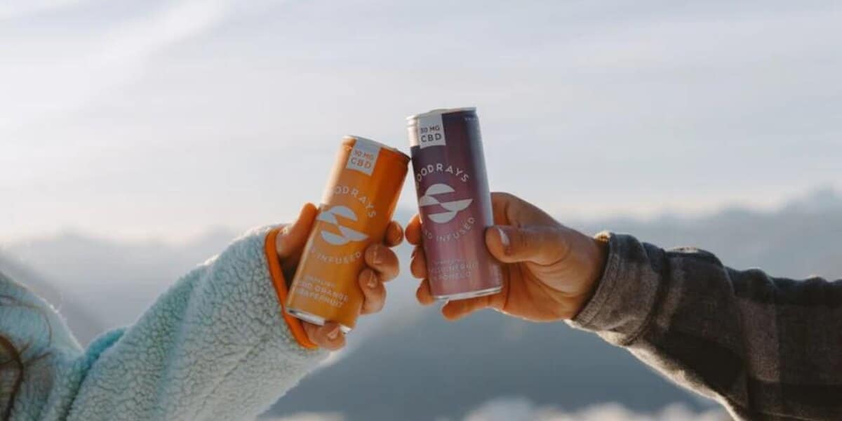 two hands cheersing cans on goodrays cbd drinks with a skyline and clouds in the background