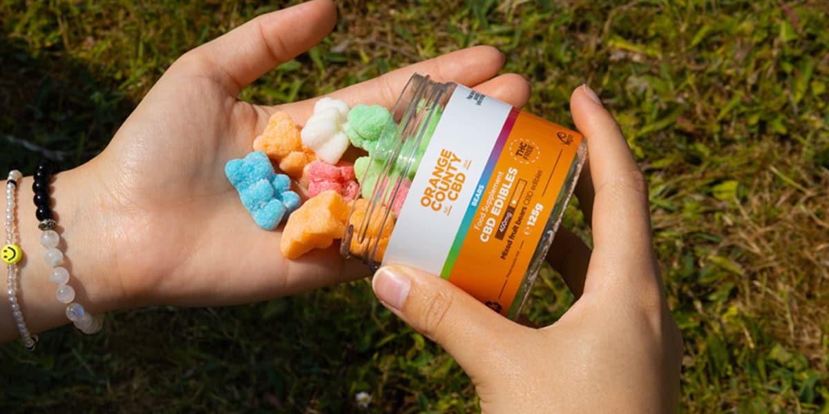 a tub of 1200mg orange county gummy bears being poured into someones hand with the sun shining and grass in the background