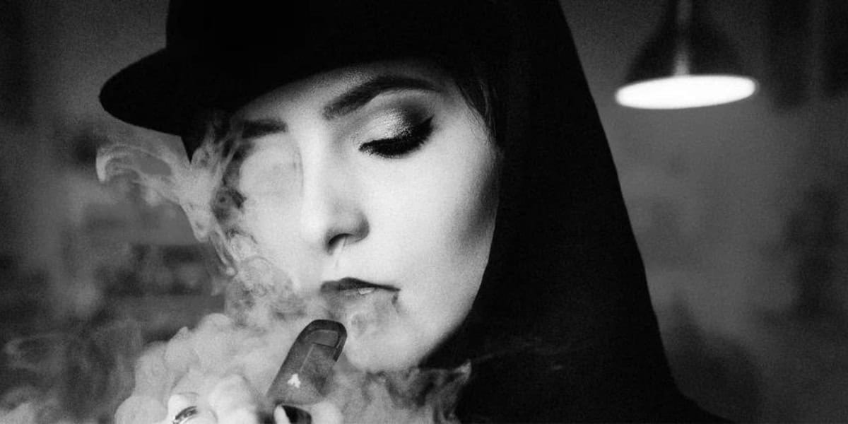 A black and white photo o a woman blowing a cloud of CBD vape