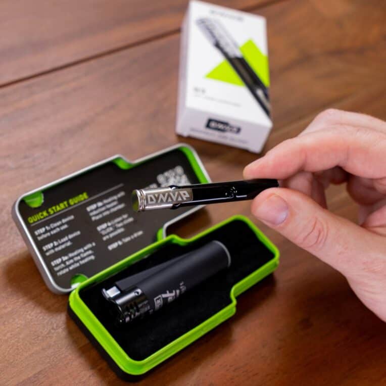 Human hand holding Dynavap G3 with packaging on table in background