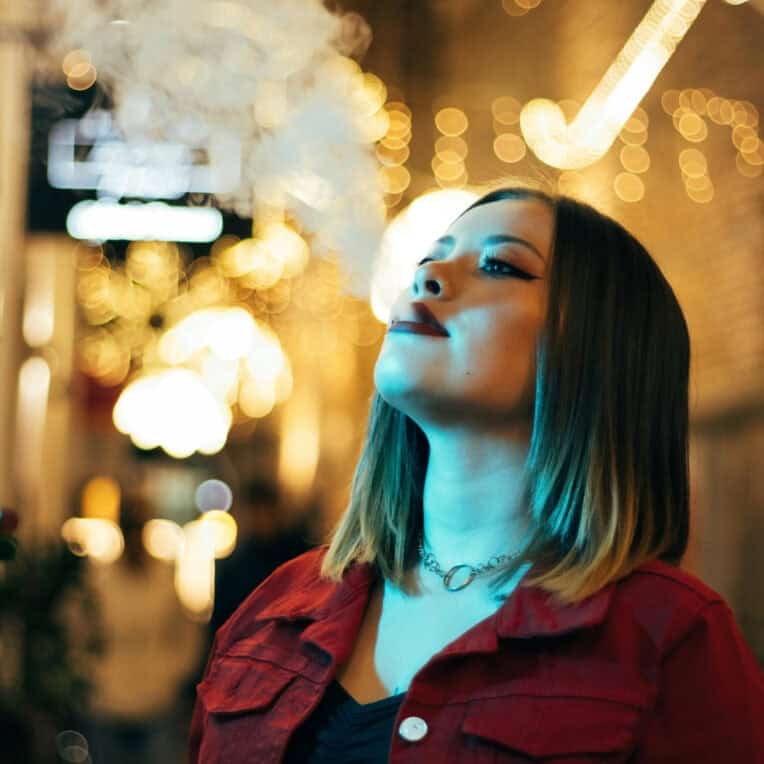 Woman vaping CBDLife Live Resin Vape Cartridge nightlife background blurred