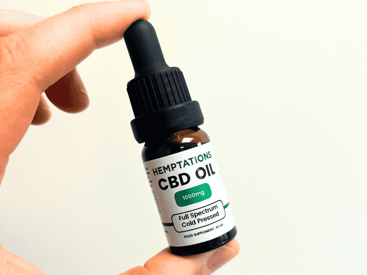 Hand holding Hemptations Cold Pressed CBD Oil 1000mg against an off-white background