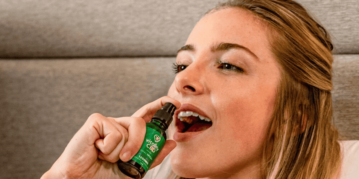 Women spraying Vitality CBD oil into her mouth while sitting on seatee or a bed
